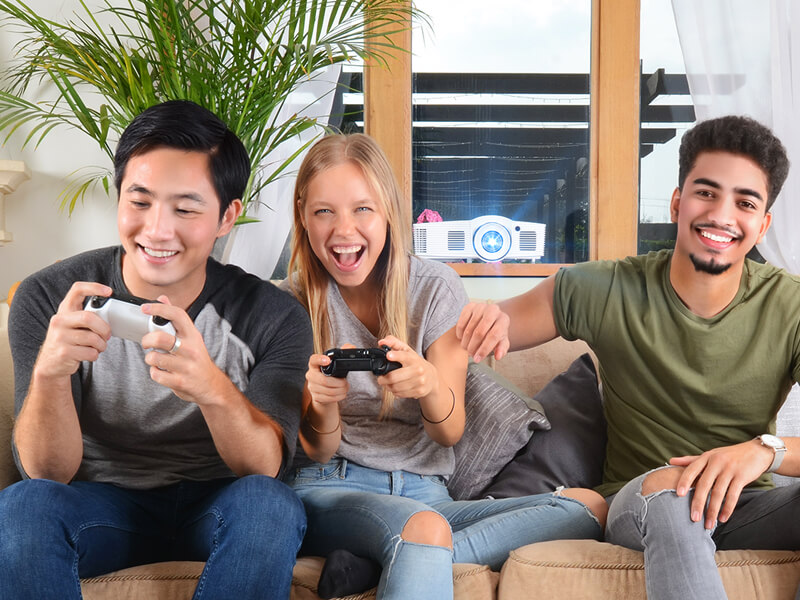 Three friends playing video games together on couch in modern living room with projecto