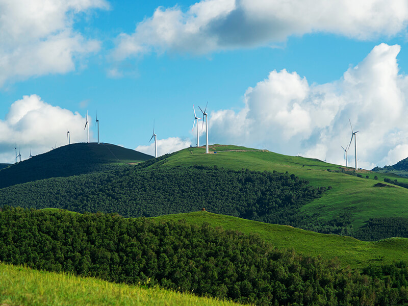 Wind turbines generating renewable energy on rolling green hills under blue sky with white clouds, showcasing sustainable power and clean energy technology
