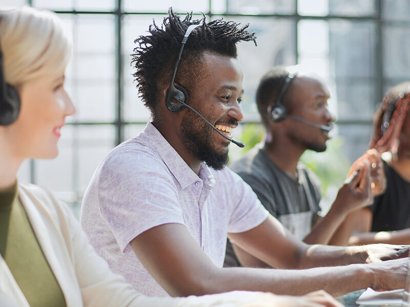 Diverse customer service team with headsets working at computers in modern office