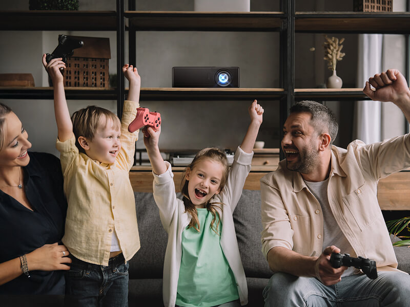 Family of four cheering with gaming controllers in modern living room with an Optoma projector behind them.