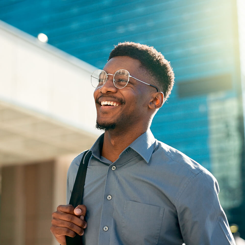 Smiling business professional with glasses carrying laptop bag outdoors representing partnership opportunities