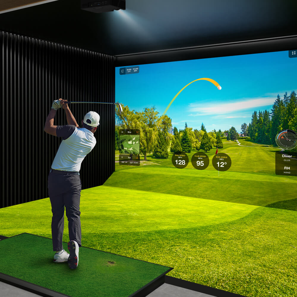 We can see the back of a golfer taking a swing. In from of them is a screen with a display that looks like a gold course. The person is standing on astro turf and we can see a dark wall to the left. There is a gold hole with a flag above it. The person is wearing a cap. Above the image we can see a  projector with light coming out of it.