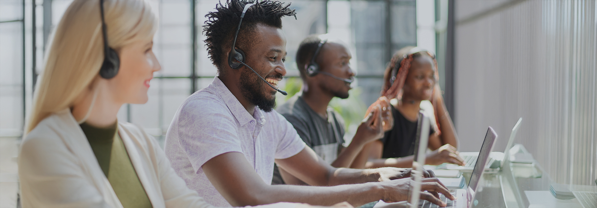 Diverse customer service team with headsets working at computers in modern office