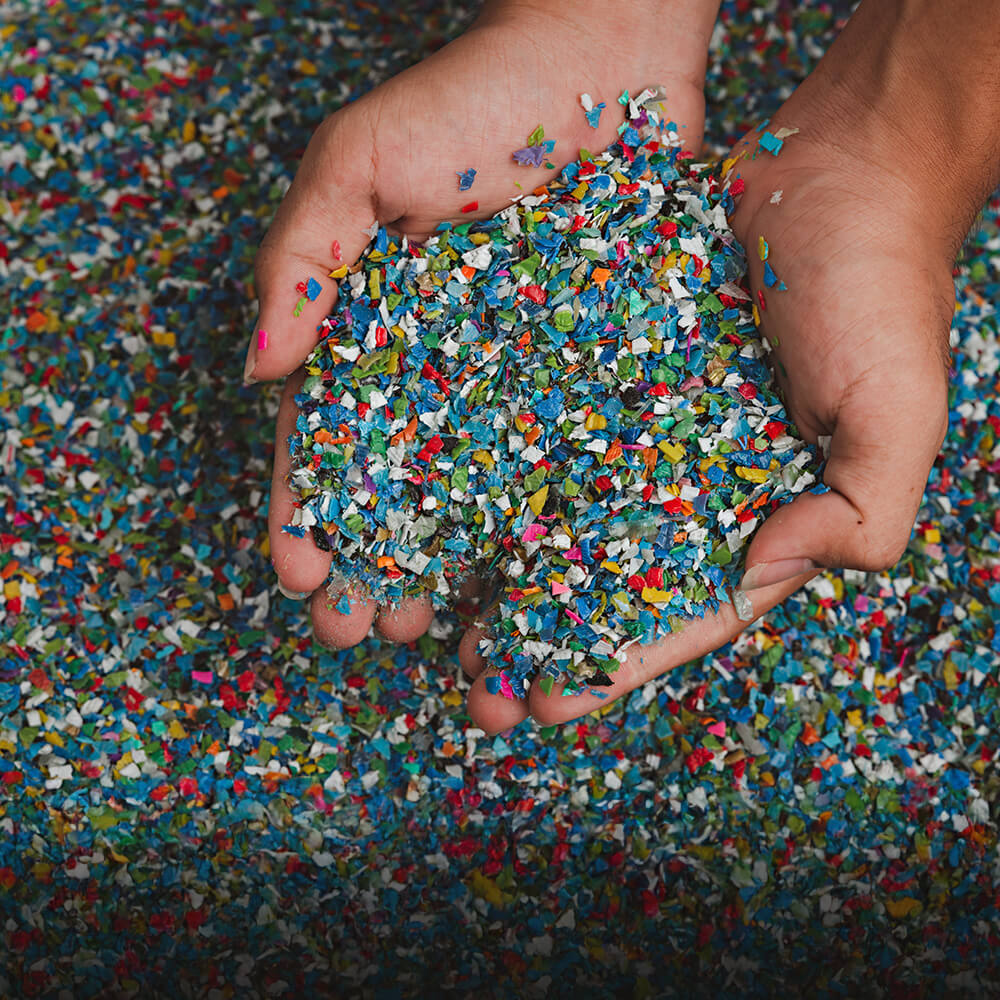 Hands holding colorful shredded plastic waste for recycling, demonstrating plastic pollution awareness and waste management solutions