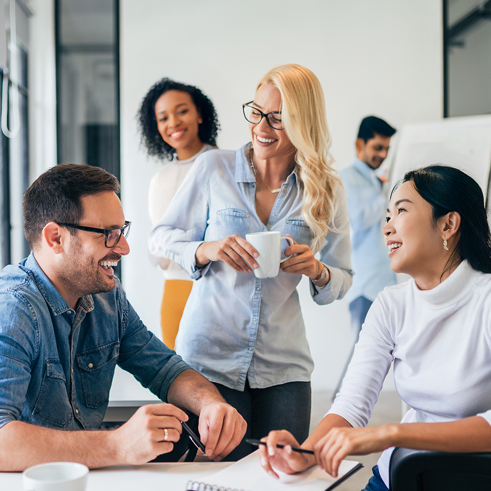 Diverse team of professionals having friendly discussion and laughing together in bright modern office workspace during casual business meeting