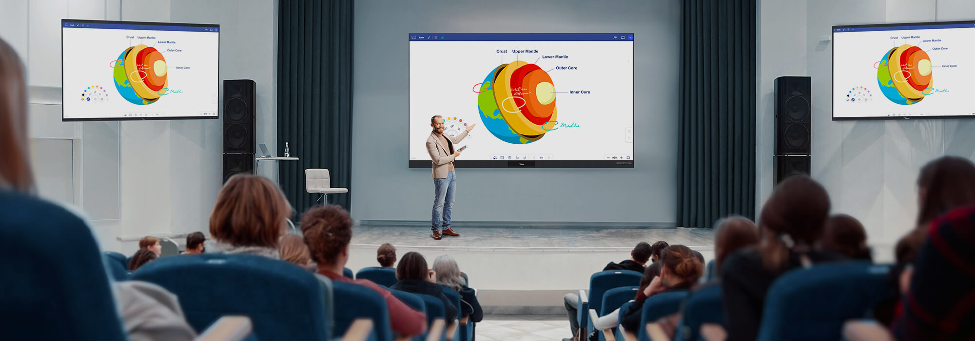 A modern conference room equipped with multiple large interactive displays showing detailed Earth science diagrams. A presenter engages with the audience while demonstrating geological layers and planetary structures on the central screen, with additional displays on either side providing supplementary visual information. The professional setup enables dynamic, educational presentations for corporate training or academic lectures.