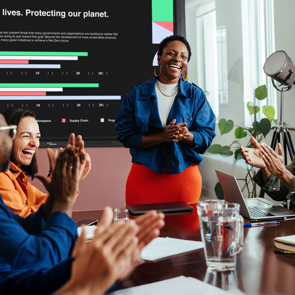 Modern office space with a group of co-working smiling and high-five in front of a large window offering great natural light.
