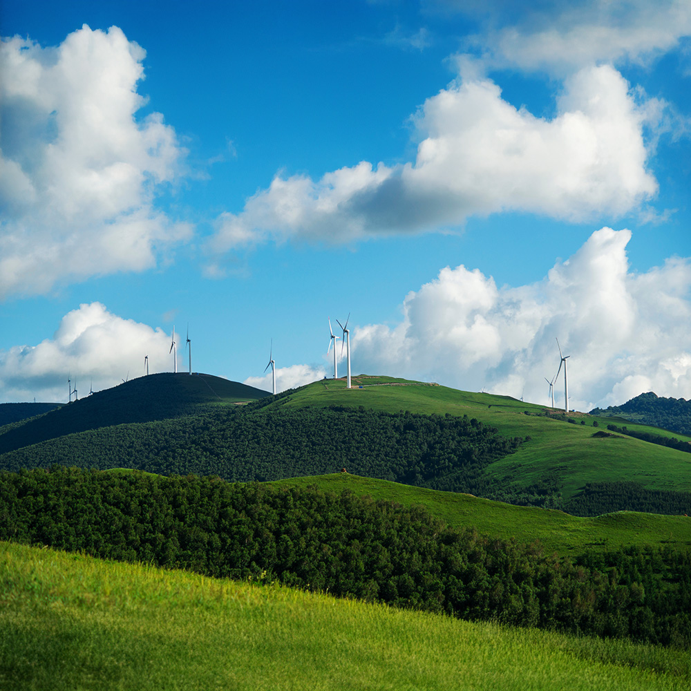 Wind turbines generating renewable energy on rolling green hills under blue sky with white clouds, showcasing sustainable power and clean energy technology
