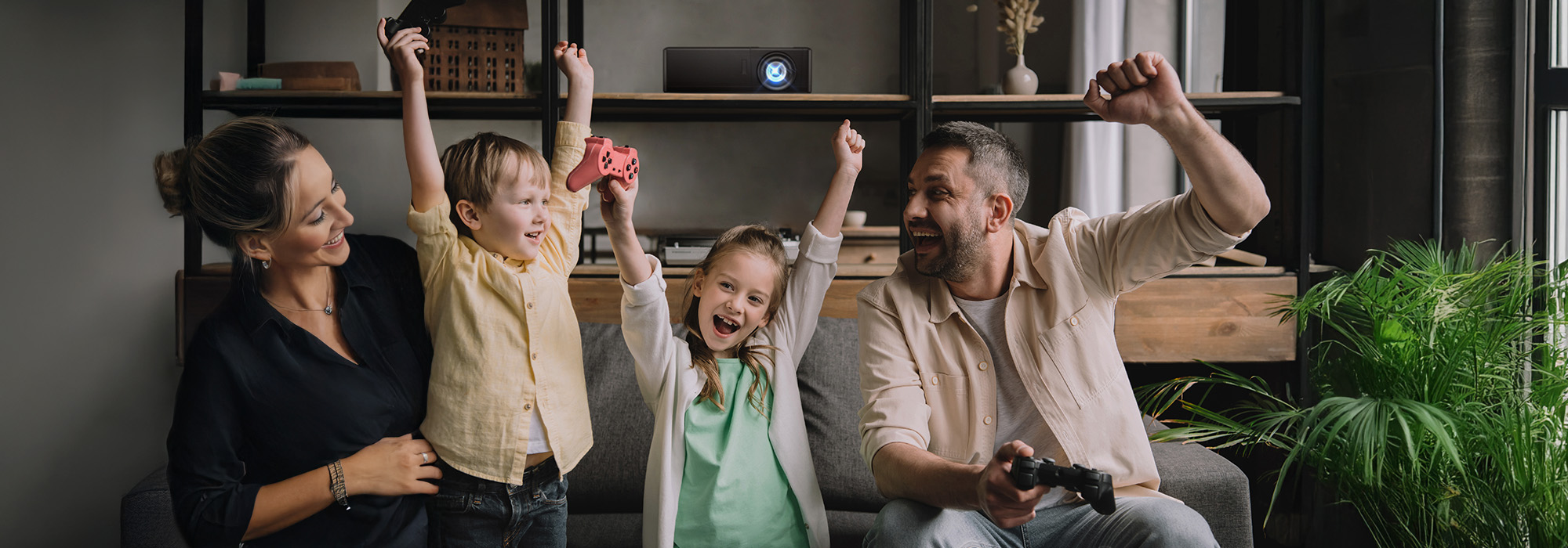 Family of four cheering with gaming controllers in modern living room with an Optoma projector behind them.