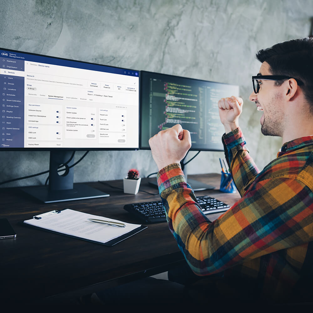 Happy software developer celebrates coding success at dual-monitor workstation with management platform.