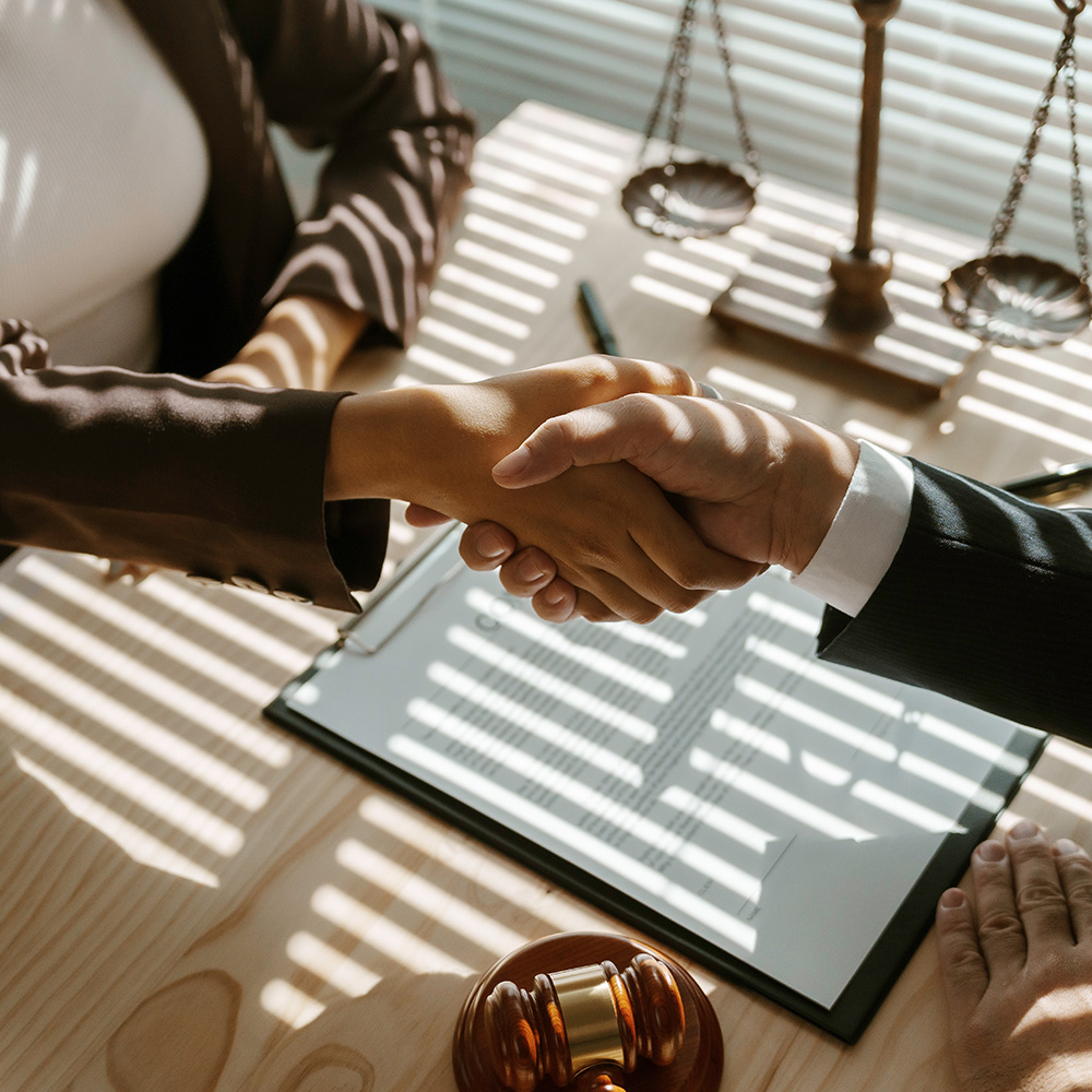Professional handshake over legal documents with scales of justice and gavel, symbolizing business compliance and legal agreement partnerships