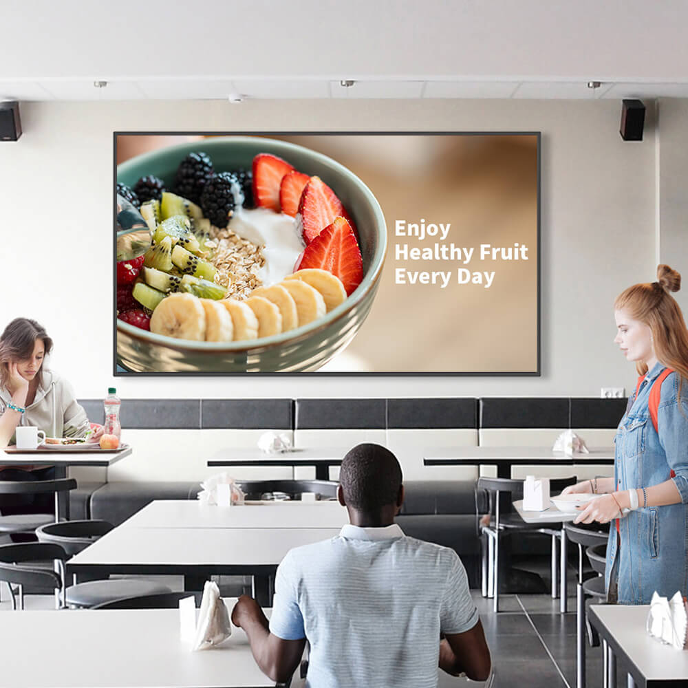 A modern cathedra that has bright lights. A person is walking by a flat panel screen which is advertising healthy food. The visual is clear and sharp.